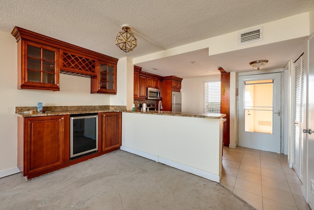 kitchen with beverage cooler, a peninsula, visible vents, appliances with stainless steel finishes, and glass insert cabinets