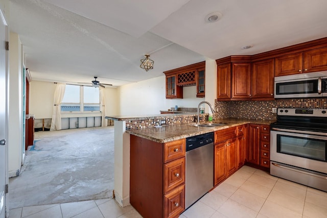 kitchen featuring stone countertops, decorative backsplash, a peninsula, stainless steel appliances, and a sink