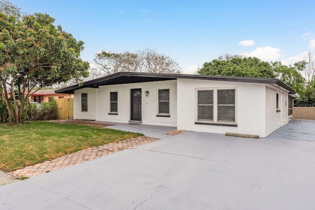 mid-century inspired home with fence, concrete block siding, and a front lawn