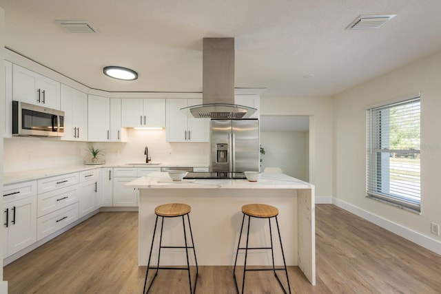 kitchen with stainless steel appliances, tasteful backsplash, visible vents, a sink, and island range hood