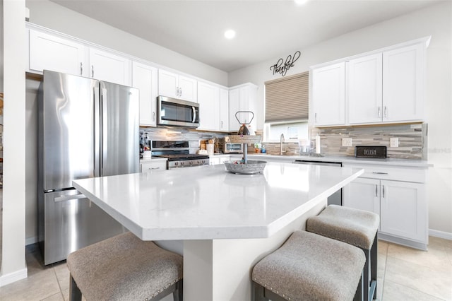 kitchen with stainless steel appliances, white cabinets, light tile patterned flooring, and a kitchen island