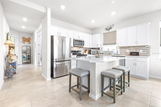 kitchen with white cabinets, a breakfast bar area, a center island, stainless steel appliances, and a sink