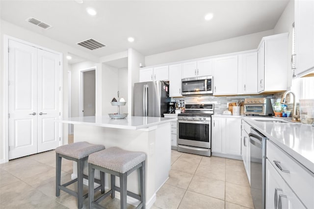 kitchen with stainless steel appliances, visible vents, a kitchen island, a sink, and a kitchen breakfast bar