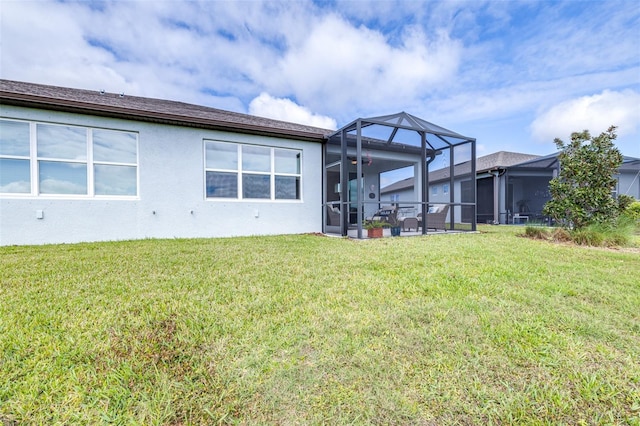 rear view of property featuring a yard, glass enclosure, and stucco siding