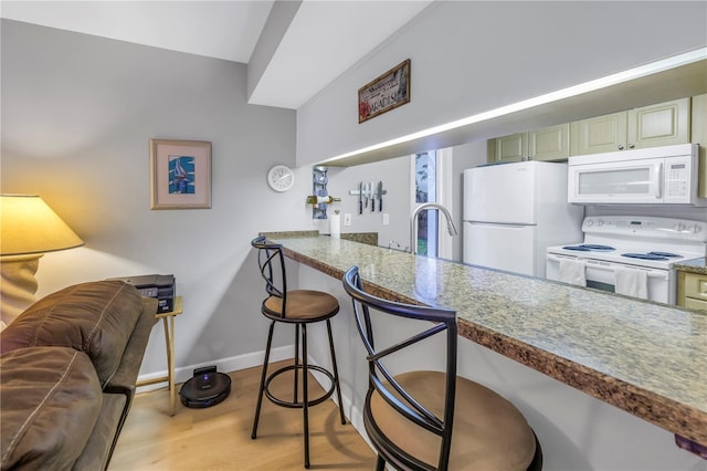 kitchen featuring white appliances, a sink, baseboards, a kitchen breakfast bar, and light wood finished floors