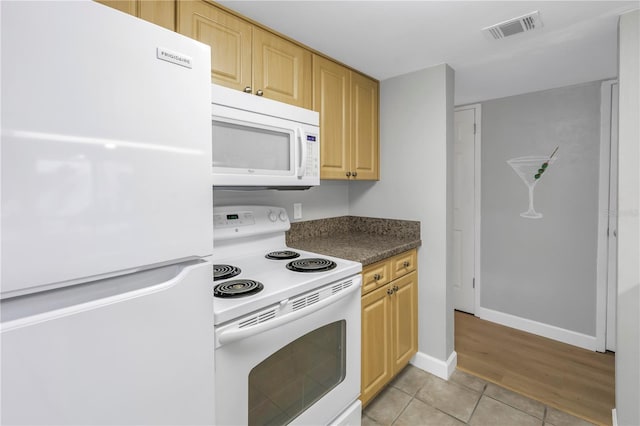 kitchen with dark countertops, white appliances, light brown cabinets, and visible vents