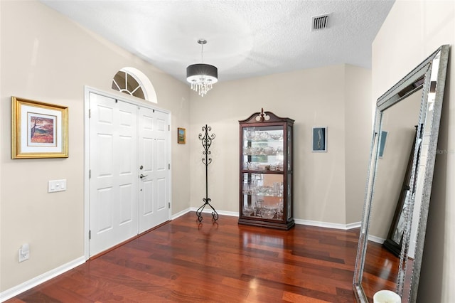 entryway with visible vents, an inviting chandelier, a textured ceiling, wood finished floors, and baseboards