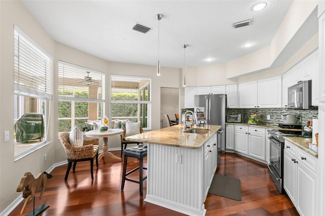 kitchen with dark wood-style flooring, stainless steel appliances, visible vents, decorative backsplash, and white cabinets