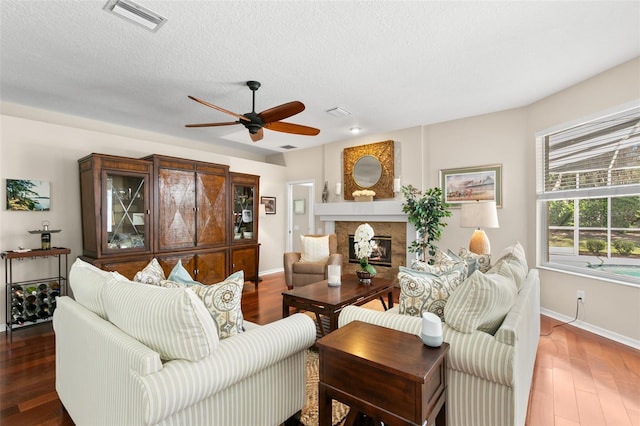 living room with a textured ceiling, wood finished floors, a glass covered fireplace, and visible vents