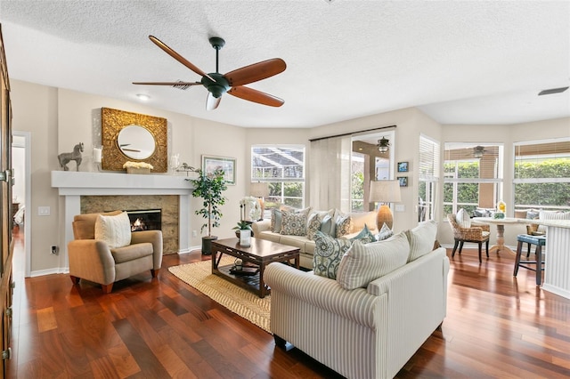 living area with a textured ceiling, ceiling fan, a glass covered fireplace, and wood finished floors