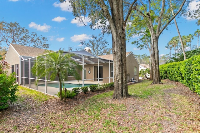 rear view of house featuring glass enclosure, a chimney, an outdoor pool, and stucco siding