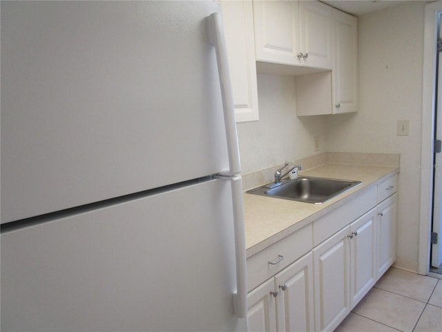 kitchen with light tile patterned floors, light countertops, freestanding refrigerator, white cabinets, and a sink