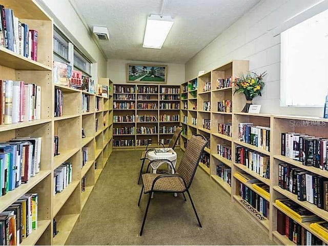 living area with wall of books, carpet flooring, and visible vents