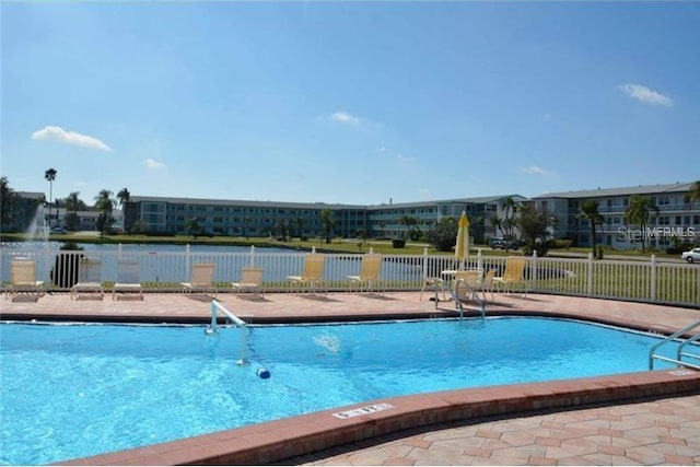 community pool with a water view, a patio area, and fence