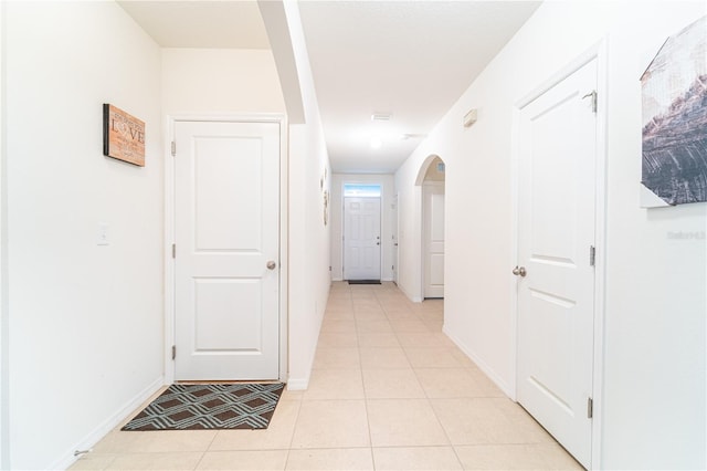 corridor with light tile patterned floors, arched walkways, and baseboards