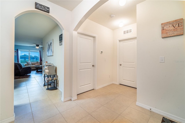 corridor with baseboards, visible vents, arched walkways, and light tile patterned flooring