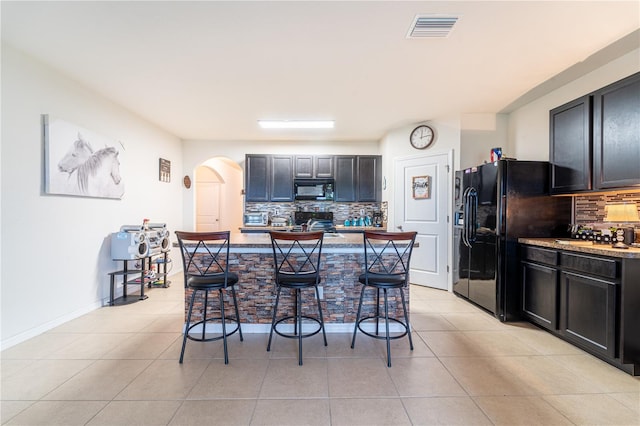 kitchen featuring arched walkways, light tile patterned floors, visible vents, black appliances, and a kitchen bar