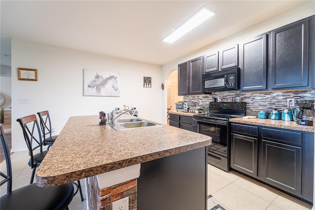 kitchen with a breakfast bar area, decorative backsplash, a kitchen island with sink, a sink, and black appliances