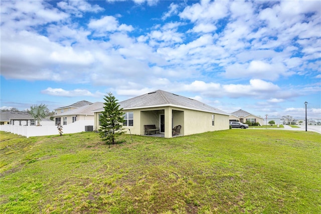 rear view of house with cooling unit, stucco siding, a yard, and fence