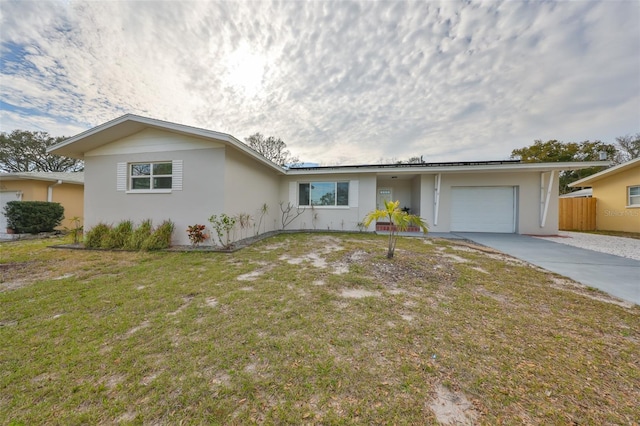 ranch-style house with solar panels, concrete driveway, an attached garage, fence, and a front lawn