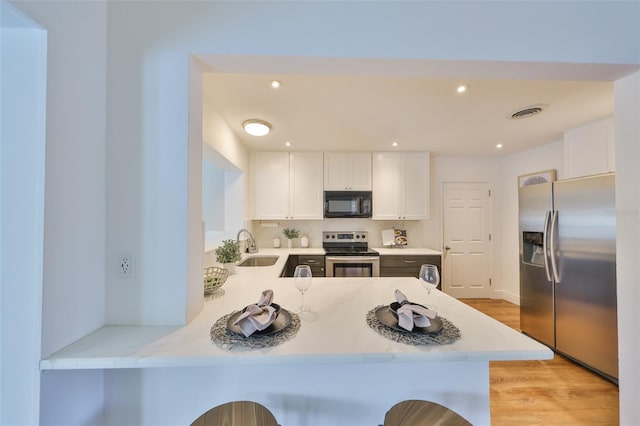 kitchen featuring appliances with stainless steel finishes, a peninsula, light stone countertops, white cabinetry, and a sink