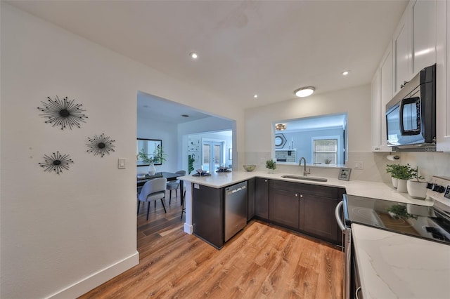 kitchen with light wood-style flooring, stainless steel appliances, a sink, white cabinetry, and light stone countertops