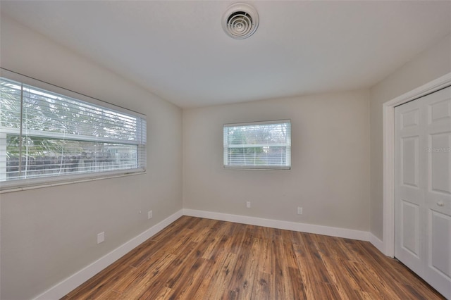 empty room with plenty of natural light, wood finished floors, and visible vents