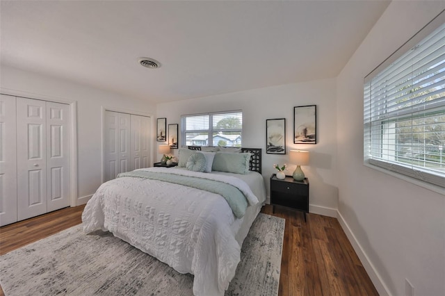 bedroom with visible vents, baseboards, multiple closets, and wood finished floors