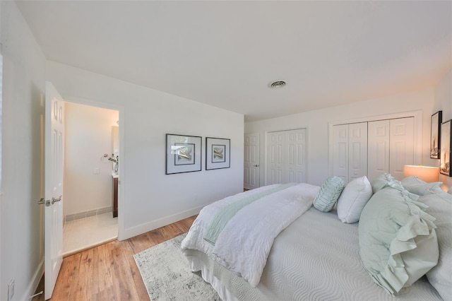 bedroom featuring light wood finished floors, baseboards, visible vents, and multiple closets