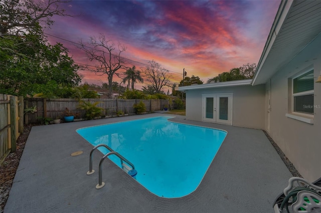 pool at dusk featuring a patio, french doors, a fenced backyard, and a fenced in pool