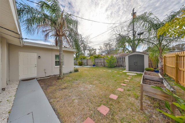 view of yard featuring a vegetable garden, a fenced backyard, an outdoor structure, and a shed