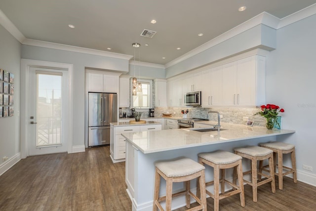 kitchen with decorative backsplash, appliances with stainless steel finishes, a peninsula, white cabinetry, and a sink