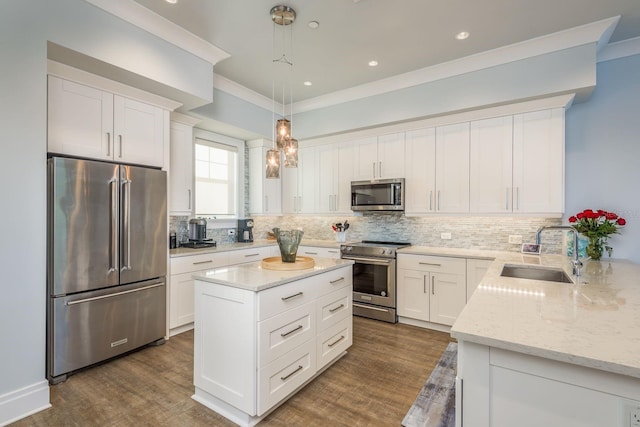 kitchen featuring light stone counters, stainless steel appliances, a sink, white cabinets, and hanging light fixtures