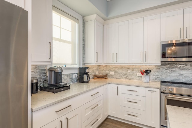 kitchen featuring light stone countertops, white cabinetry, stainless steel appliances, and decorative backsplash