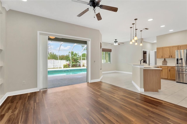 kitchen with stainless steel refrigerator with ice dispenser, open floor plan, light wood finished floors, ceiling fan, and light countertops