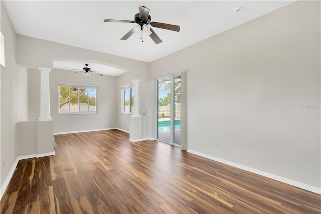 empty room with a wealth of natural light, wood finished floors, a ceiling fan, and ornate columns