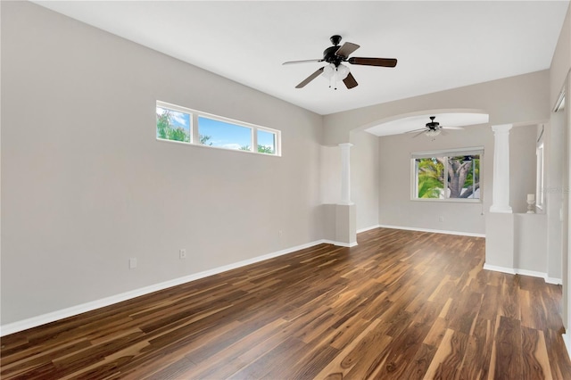 unfurnished room with a wealth of natural light, a ceiling fan, dark wood-style flooring, and ornate columns