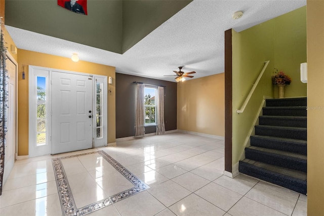 tiled foyer with a ceiling fan, stairs, baseboards, and a textured ceiling