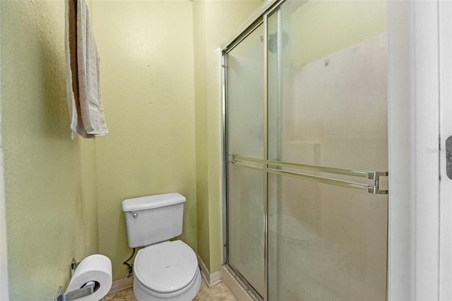 full bathroom with toilet, a stall shower, and baseboards