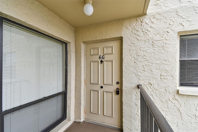 view of exterior entry with a balcony and stucco siding