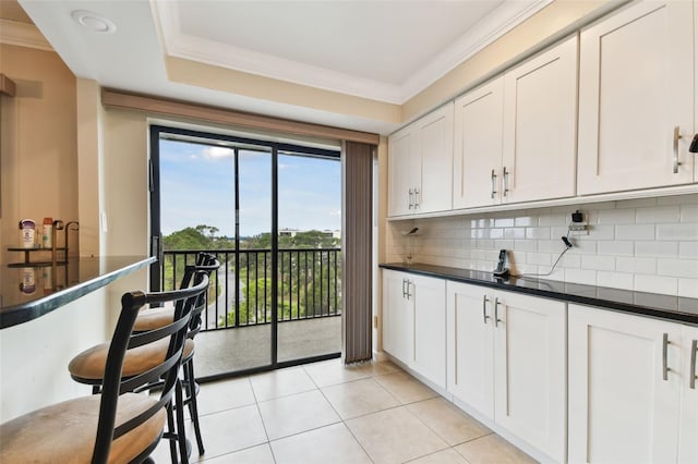 kitchen featuring crown molding, light tile patterned floors, dark countertops, decorative backsplash, and white cabinetry