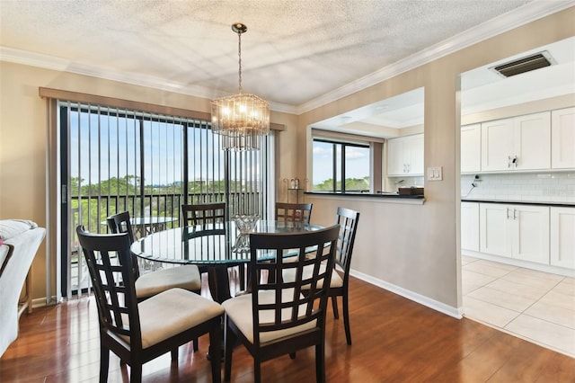 dining space with an inviting chandelier, visible vents, wood finished floors, and ornamental molding