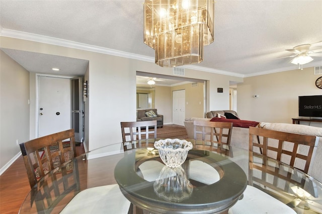 dining space featuring a textured ceiling, ornamental molding, ceiling fan with notable chandelier, and dark wood finished floors