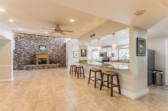 kitchen featuring a peninsula, a fireplace, white cabinets, appliances with stainless steel finishes, and decorative light fixtures