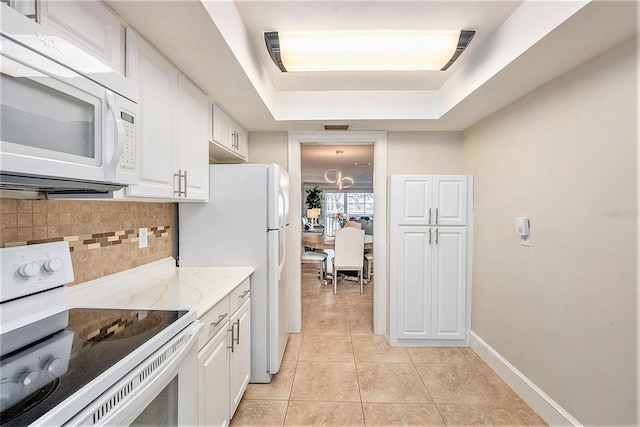 kitchen with a tray ceiling, white appliances, backsplash, and white cabinets