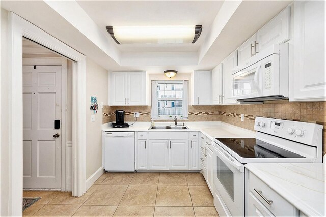 kitchen with white appliances, light tile patterned floors, a tray ceiling, a sink, and backsplash