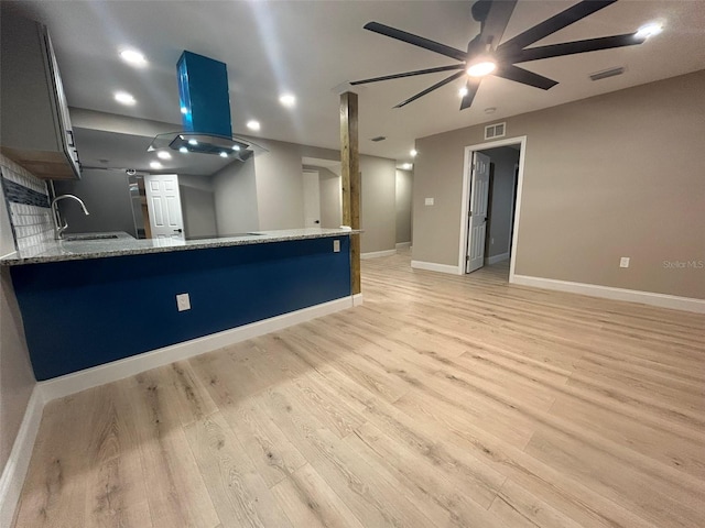 kitchen featuring visible vents, island range hood, a peninsula, light stone countertops, and a sink