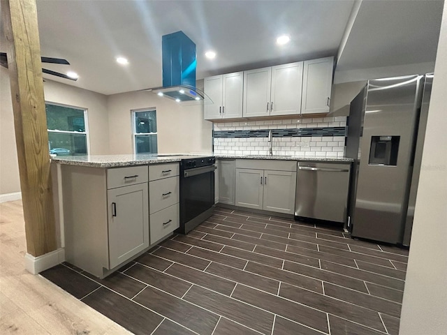 kitchen featuring light stone counters, island range hood, stainless steel appliances, a peninsula, and a sink