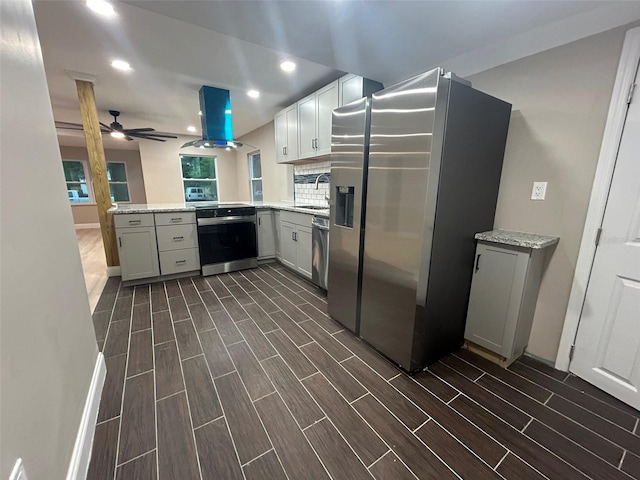 kitchen with a peninsula, island exhaust hood, stainless steel appliances, wood finish floors, and a sink