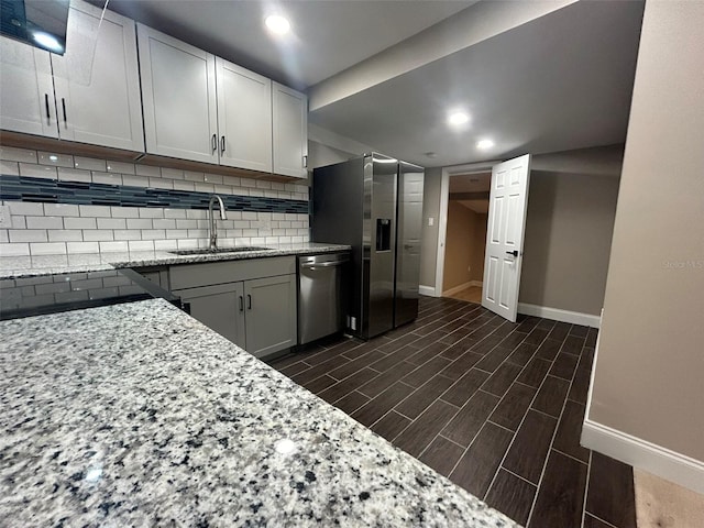 kitchen with tasteful backsplash, white cabinets, light stone counters, stainless steel appliances, and a sink